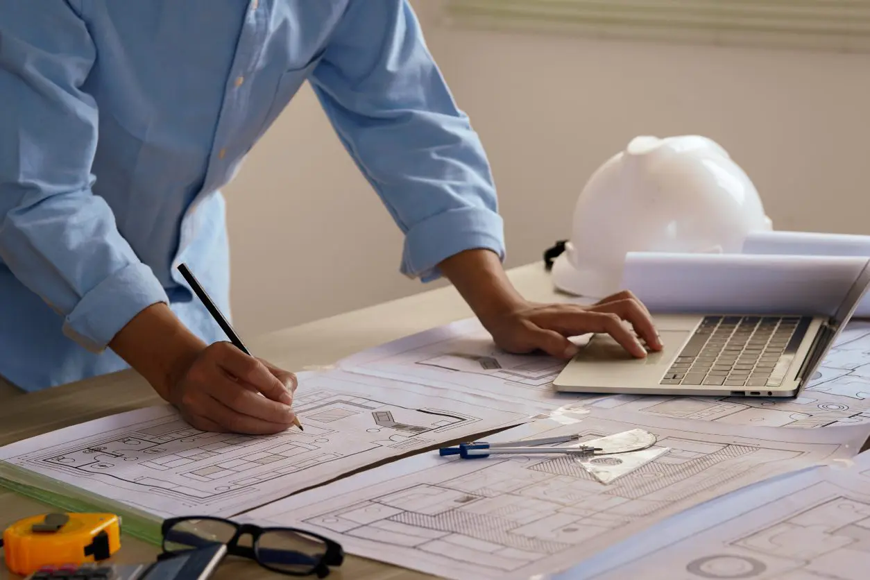 Architect drawing plans on desk with laptop.