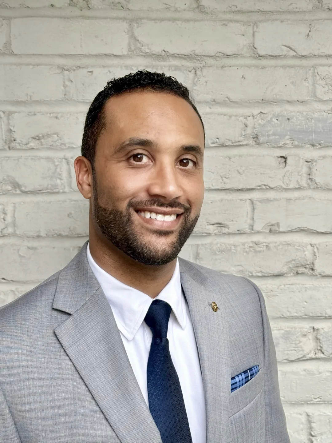 Professional man smiling in a suit against a brick wall.